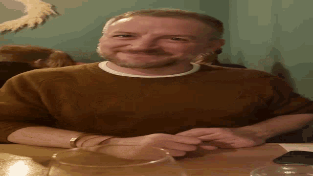 a man in a brown sweater is smiling and sitting at a table