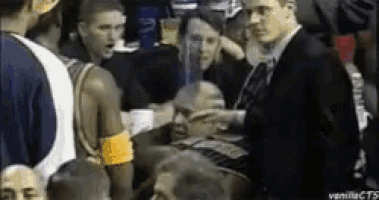 a man in a suit is talking to a basketball player in a crowd