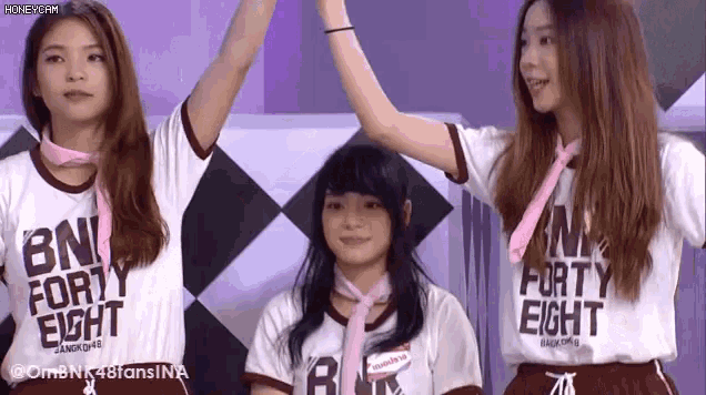three girls are standing next to each other with their arms in the air and wearing shirts that say bn forty eight .