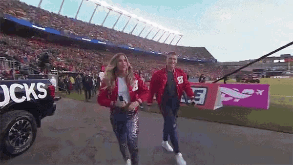 a man and a woman are walking out of a stadium with a truck that says cks on it