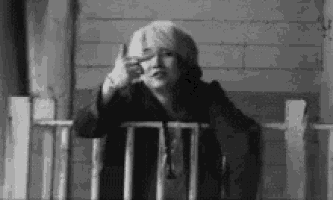 a woman is sitting on a porch making a peace sign .