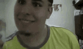 a man in a yellow shirt is smiling in a room with a picture of a woman on the wall