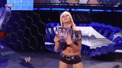 a female wrestler holds a trophy in front of a large screen that says wwe