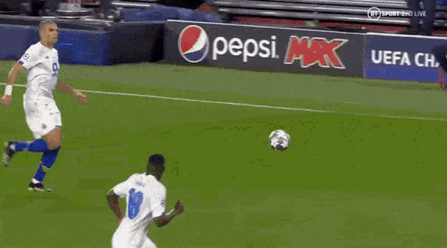 a soccer player is kicking a soccer ball while another player tries to block it .