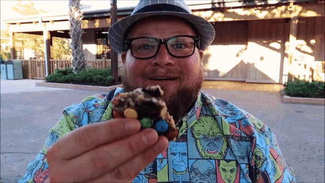 a man wearing glasses and a hat is holding a piece of cake