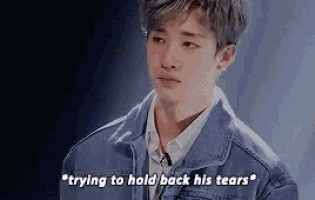 a young man wearing a denim jacket is crying and saying " trying to hold back his tears "