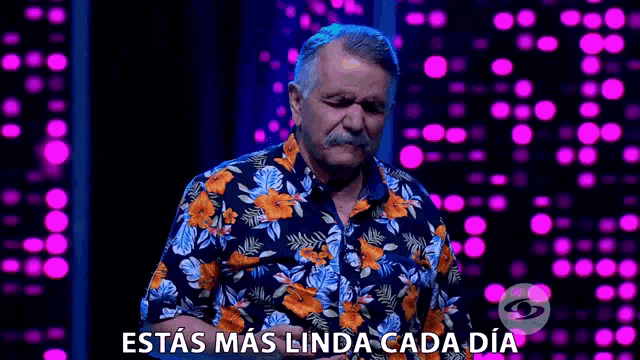 a man with a mustache wearing a floral shirt is standing in front of a colorful background .