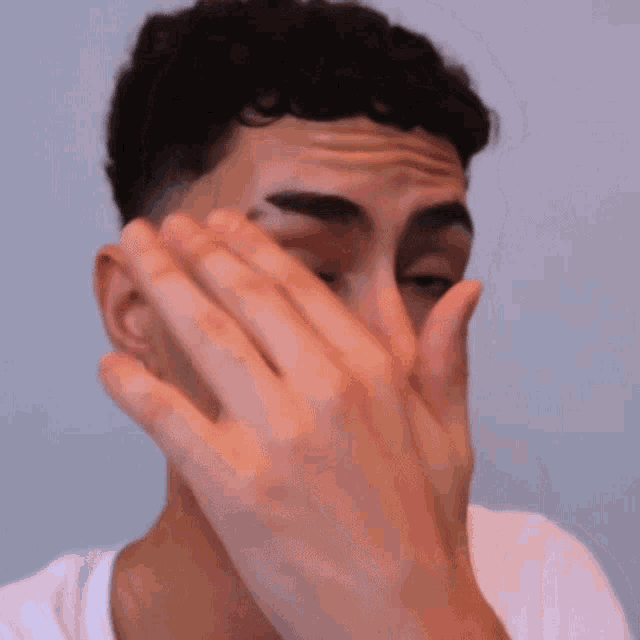a young man covering his face with his hand while wearing earrings