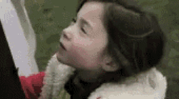 a little girl is looking up at something in the sky while wearing a fur coat .