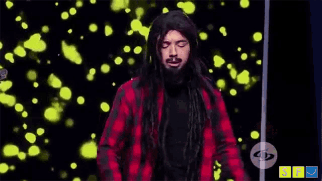 a man with long dreadlocks and a beard is standing in front of a yellow background .