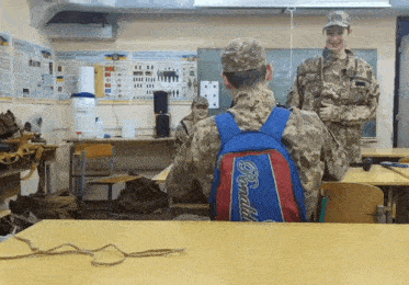 two soldiers in a classroom with one wearing a backpack that says donald