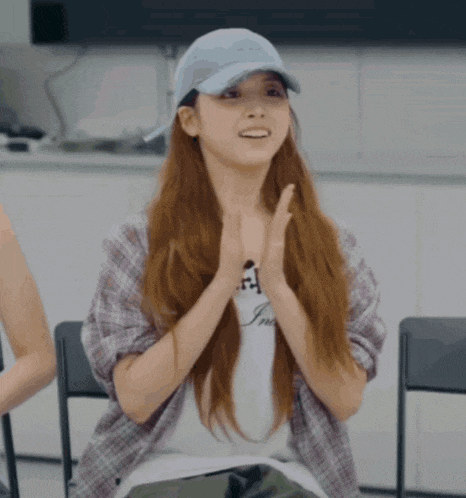 a woman wearing a baseball cap and a plaid shirt is smiling with her hands folded