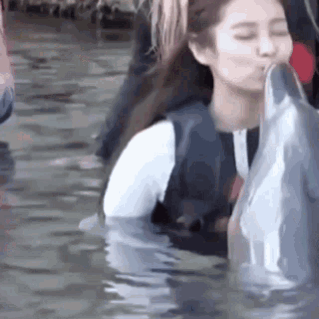 a woman is kissing a dolphin on the nose while swimming in the water .