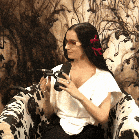 a woman sitting in a cow print chair holding a microphone with a ring on her finger