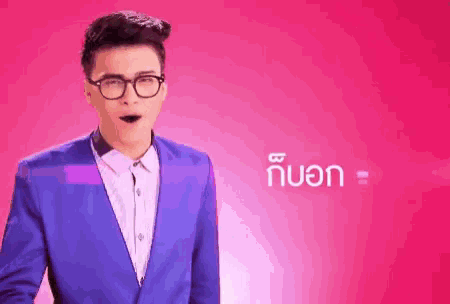 a young man in a blue suit and glasses is standing in front of a pink background .