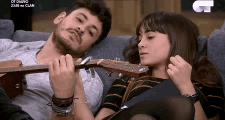 a man is playing a guitar to a woman on a couch .