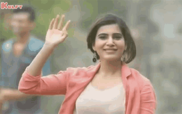 a woman in a pink jacket is waving her hand in front of a man .