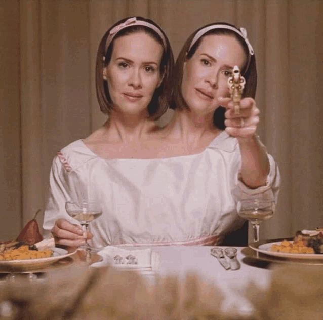 two women are sitting at a table holding a gun and a glass of wine