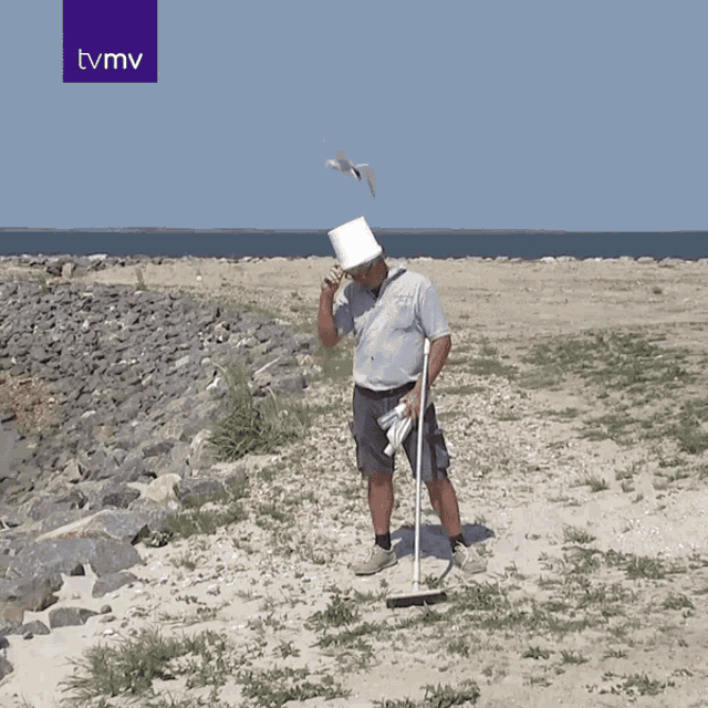 a man with a bucket on his head is standing on a beach with a tvmv logo above him