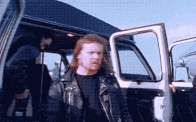 a man in a leather jacket is walking out of a van