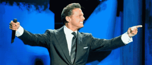 a man in a suit and tie holds a microphone and points