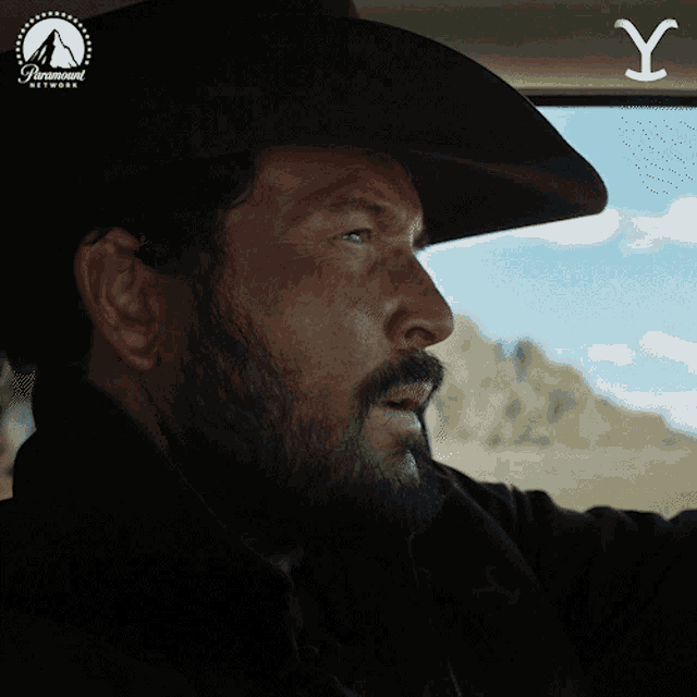 a man wearing a cowboy hat is driving a car with a paramount network logo behind him
