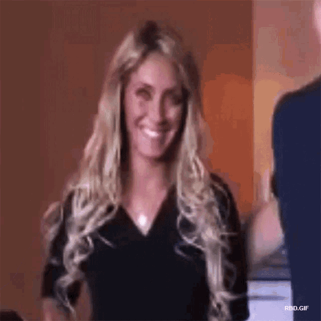 a woman with long blonde hair is smiling while standing next to a man in a room .