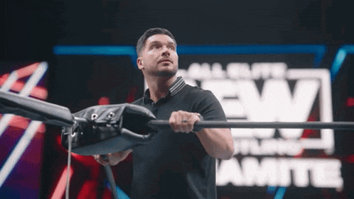 a man in a black shirt is holding a bar in front of a screen that says all elite wrestling