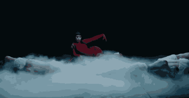 a woman in a red bodysuit is laying on the ground in a cloud of smoke