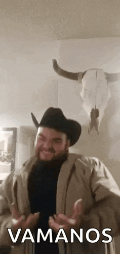 a man wearing a cowboy hat and a coat is standing in front of a bull skull .