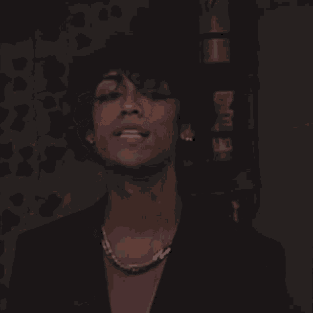 a man wearing a necklace and a ring looks at the camera