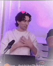 a man in a white shirt is standing in front of a microphone with a heart on his head .