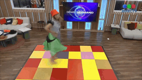 a woman is dancing on a dance floor in front of a tv screen that says gran hermano