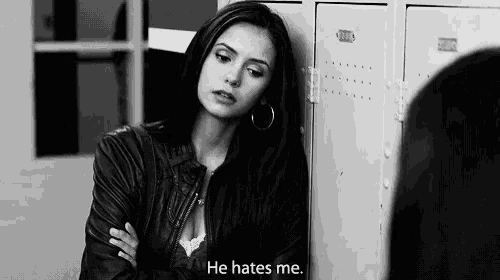 a black and white photo of a woman leaning against a locker with the words he hates me .