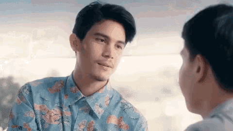a man in a blue shirt is looking at another man in a floral shirt .