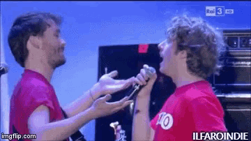 a man in a red shirt with the number 10 on it is singing into another man 's microphone