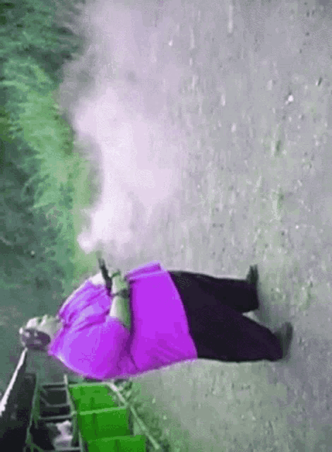 a man in a purple shirt is laying on the ground smoking a cigarette