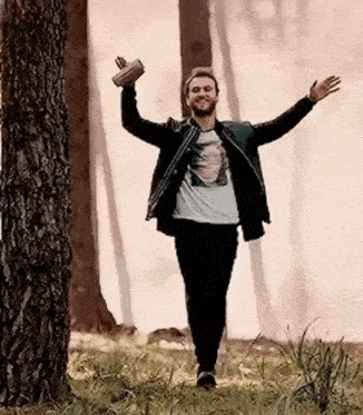 a man is standing in a field with his arms outstretched in front of trees .