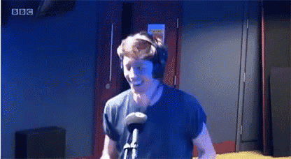 a man wearing headphones and a microphone is dancing in front of a bbc logo .