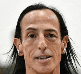 a man with long black hair and hoop earrings is smiling for the camera .