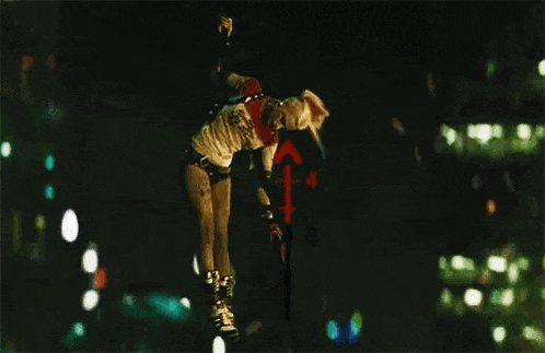 a woman in a suicide squad costume is flying through the air in the dark .