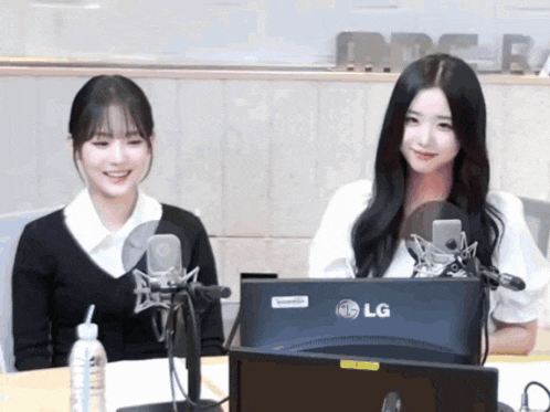 two girls are sitting in front of an lg computer