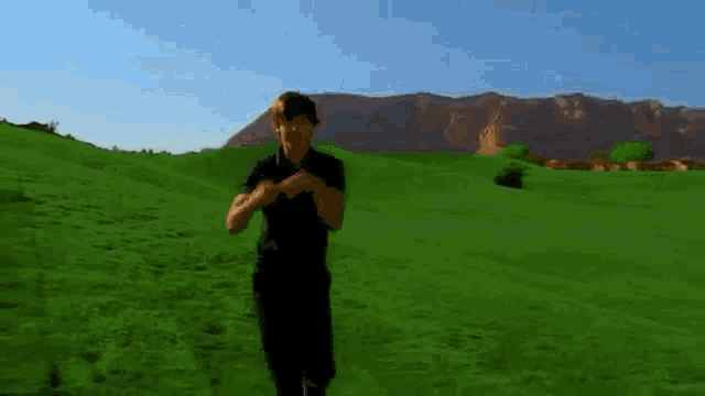 a man in a black shirt is standing in a grassy field .