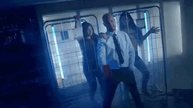 a man in a white shirt and tie is dancing with two women in a dark room .