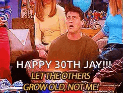 a man is sitting on a couch with a group of people and says `` happy 30th jay !!! ``