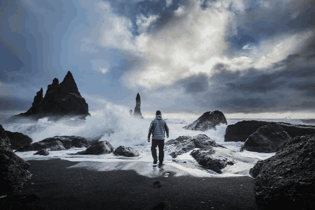 a man standing on a rocky beach looking at a stormy ocean