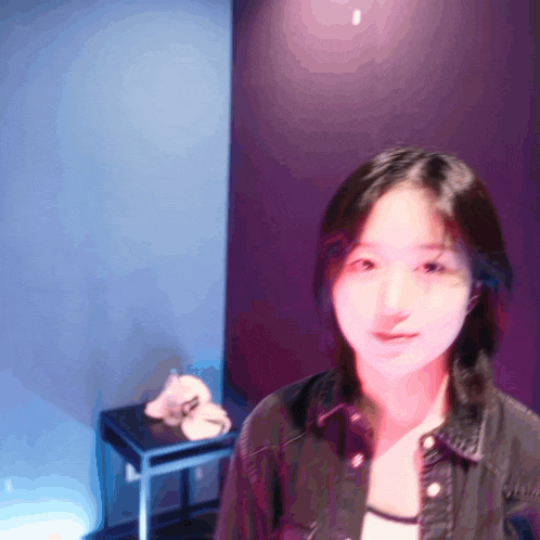 a woman in a denim jacket stands in front of a blue wall