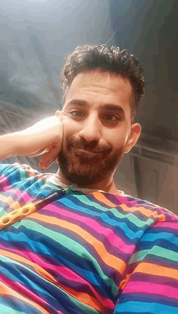 a man with a beard wearing a colorful striped shirt looks at the camera