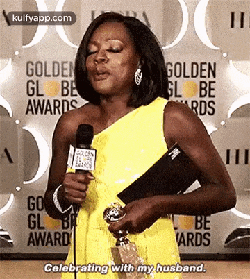 a woman is holding a trophy and talking into a microphone at the golden globe awards .