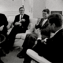 a group of men in suits and ties are sitting on a couch smoking cigarettes .